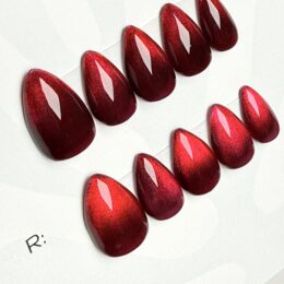 Crimson Reign red magnetic cat-eye press-on nails in short stiletto, full set of 10 Close-up of red cat-eye gel shimmer on Crimson Reign press-on nails Crimson Reign press-ons on HoneyBae Nailz sizing card Dark red magnetic gel press-on nails with glossy finish